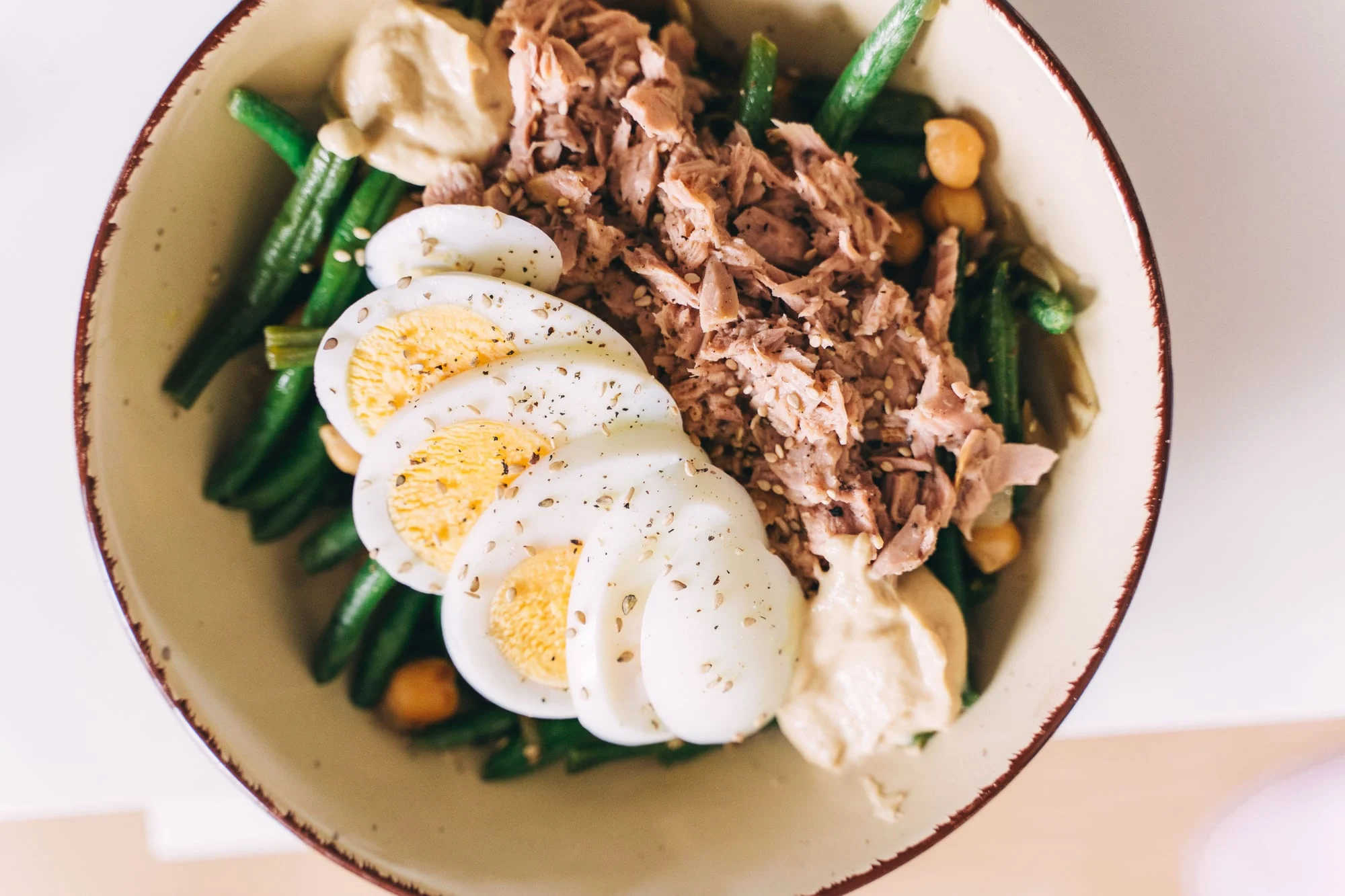 A bowl of eggs, tuna, green beans and hummus.